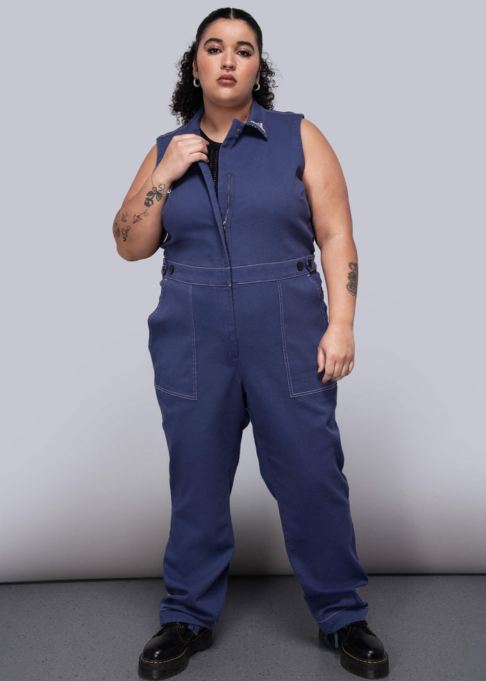 1X=Woman wearing a blue denim jumpsuit against a plain background
