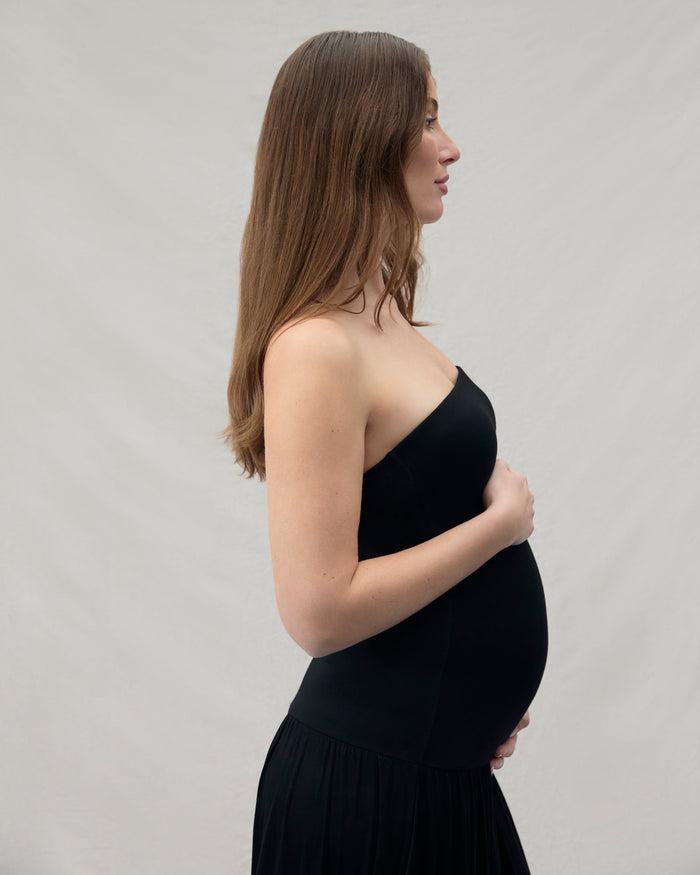 Pregnant woman wearing a black dress against a plain background