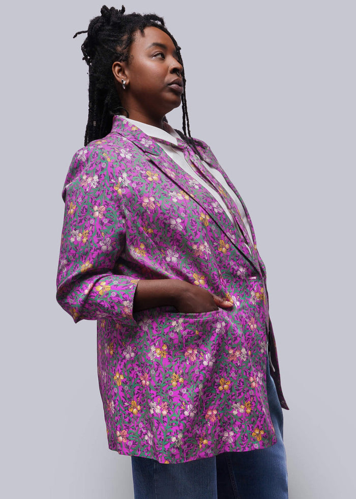 1X=Person wearing a purple floral blazer and blue jeans against a white background