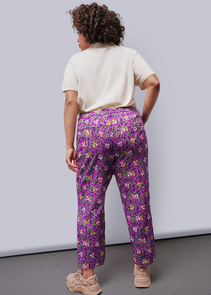 1X=Back of person wearing a white sweater and purple floral pants against a plain background
