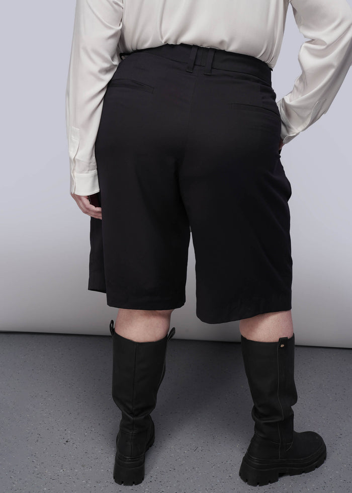 1X=Person wearing black shorts and black boots from behind on a plain background