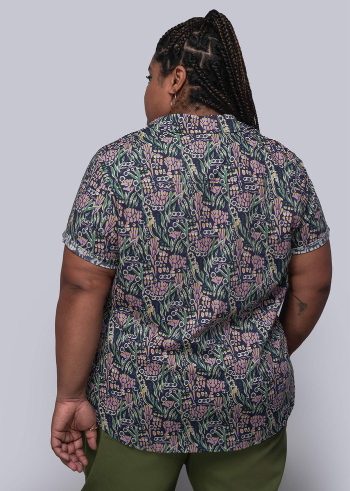 1X=Person wearing a patterned shirt and green pants against a plain background
