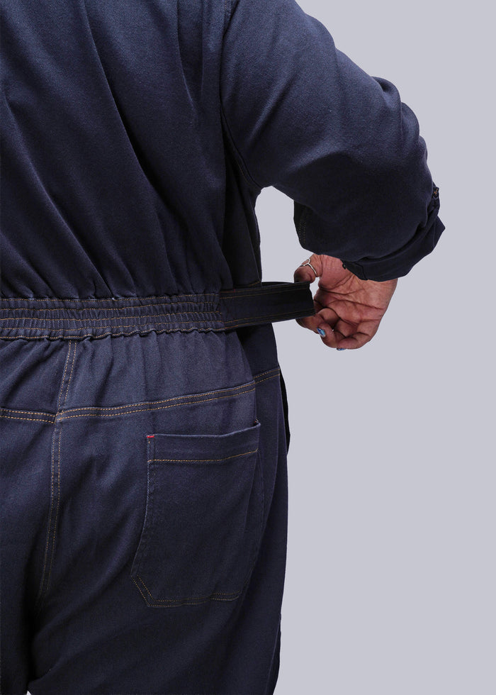 1X=Person wearing a navy blue denim jumpsuit against a grey background