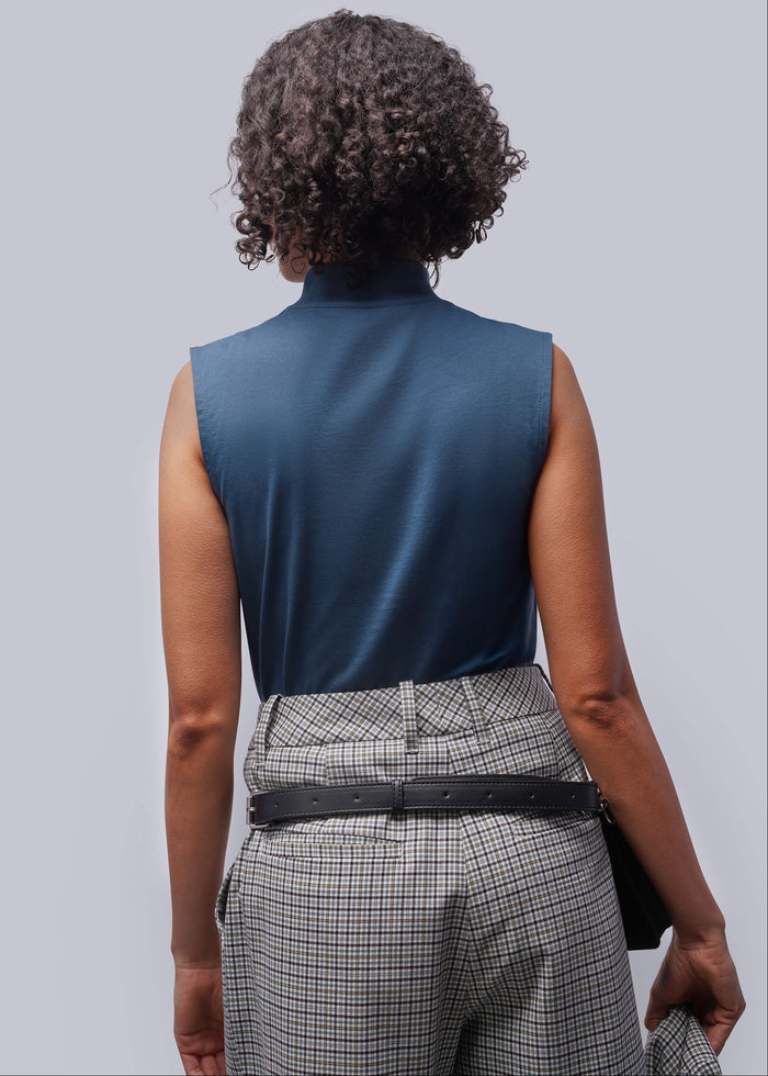 S=Person wearing a blue sleeveless top and plaid pants on a light gray background