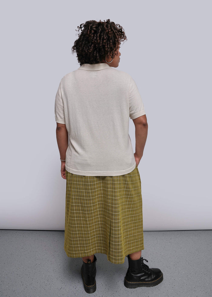 1X=Person wearing a white t-shirt and yellow plaid skirt against a plain background