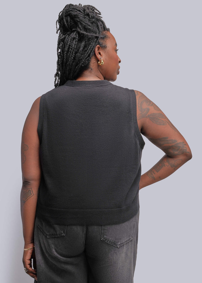 1X=A person shown from the back wearing a black gray sleeveless top and gray jeans against a light gray studio background.
