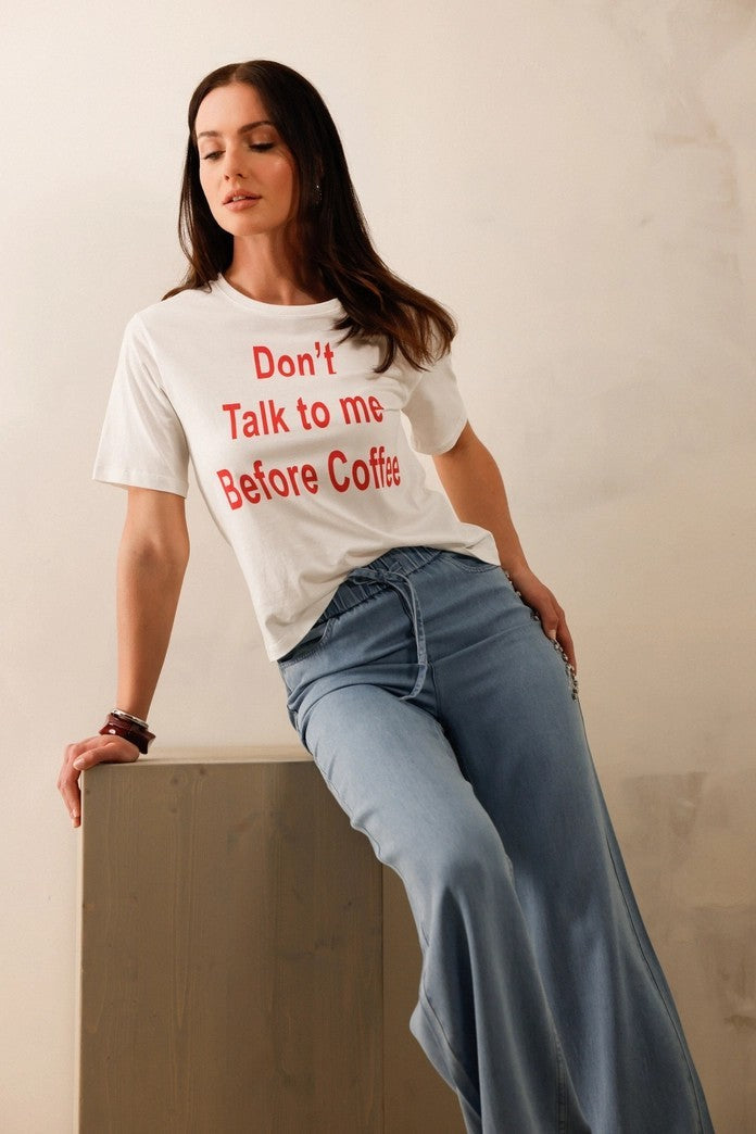 Woman wearing a white t-shirt with red text and blue jeans, leaning against a neutral background.