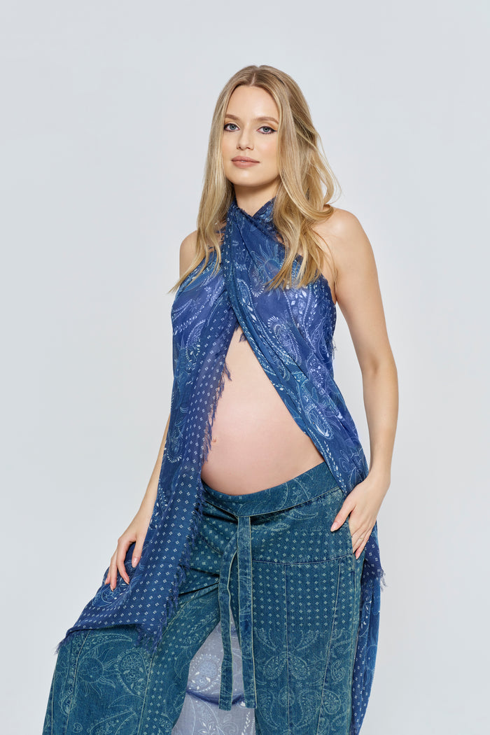 Pregnant woman wearing a blue patterned scarf and jeans outfit from Bumpsuit on a white background