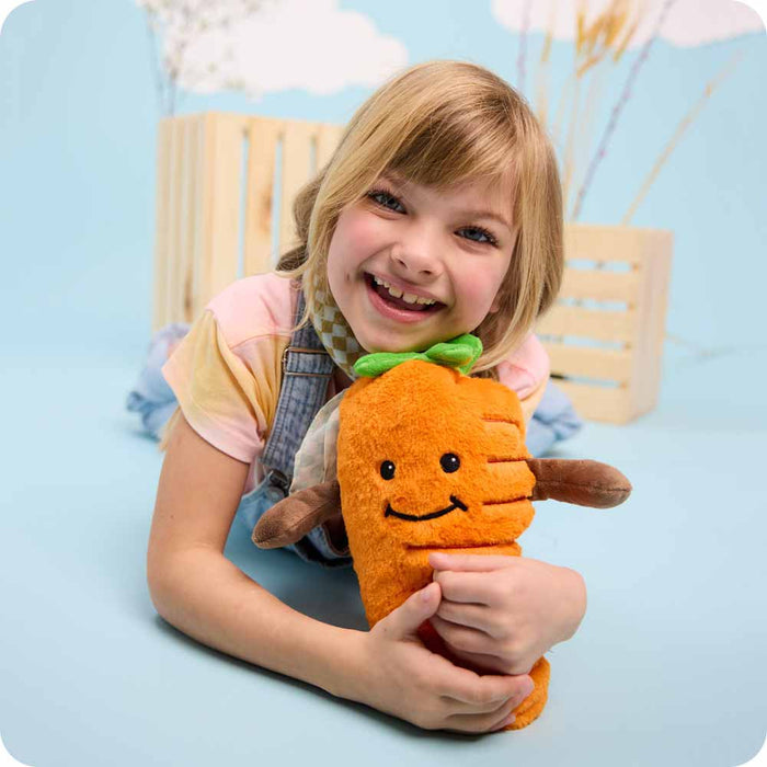 Little girl laying flat on the floor while hugging a Carrot Warmies