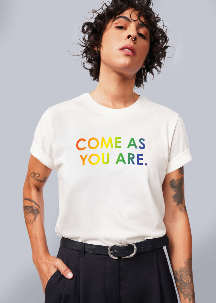 S=Person wearing a white t-shirt with 'COME AS YOU ARE' text in colorful letters against a gray background