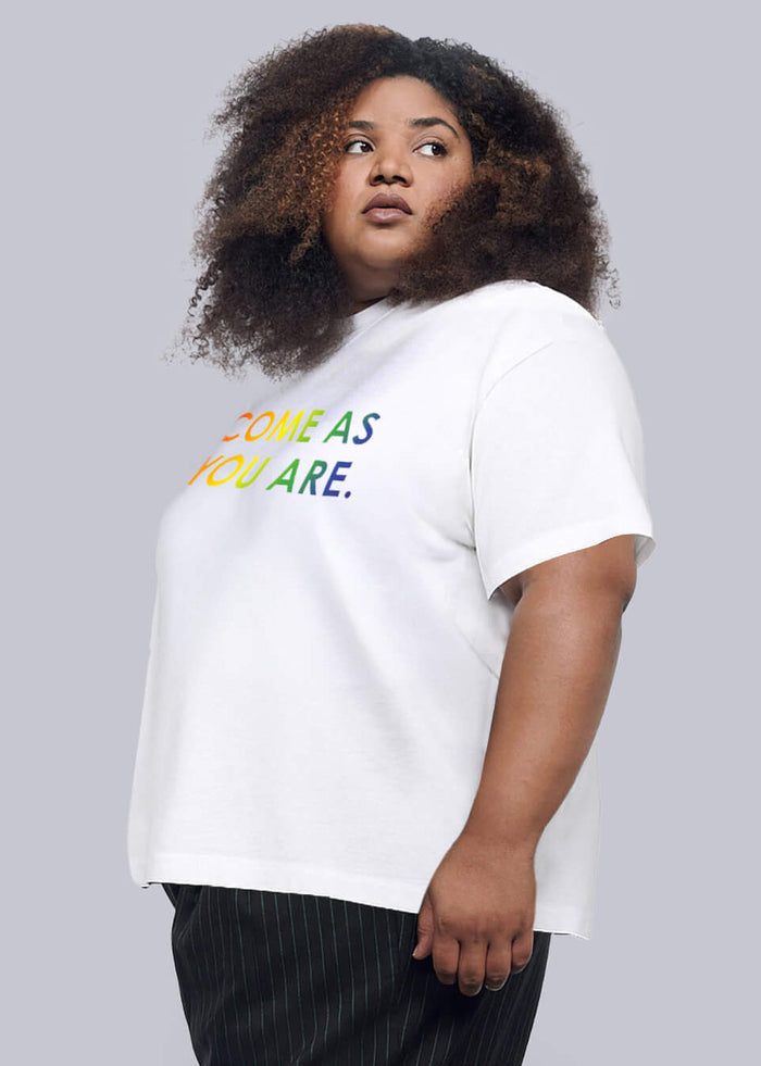 1X=Person wearing a white t-shirt with colorful text and black pants on a plain background
