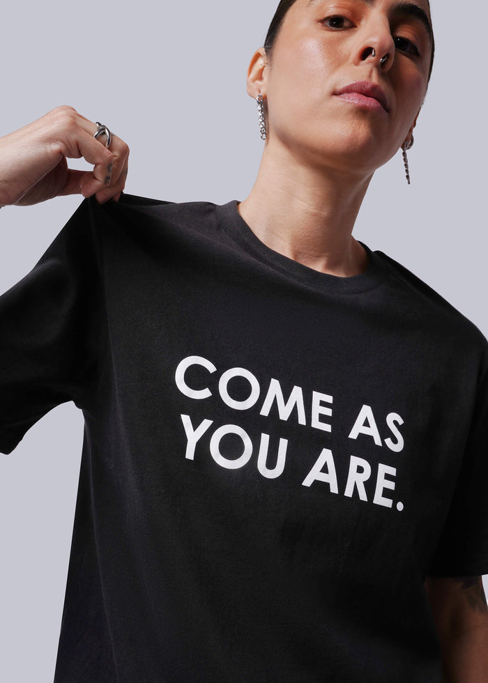 S=Person wearing a black t-shirt with 'COME AS YOU ARE' text on a plain background