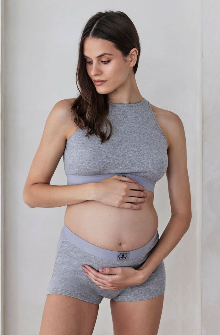 Pregnant woman wearing a grey cotton rib crop top and boy shorts set against a plain background