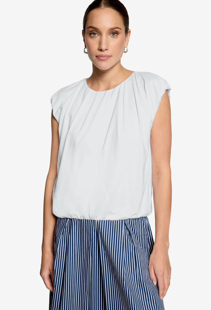 Woman wearing a white sleeveless top and blue striped pants on a white background