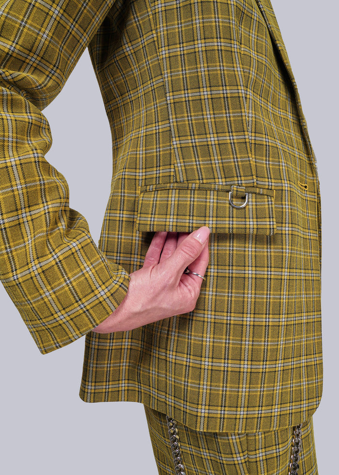 S=Close up of yellow plaid blazer with a hand touching the pocket flap on a light gray background