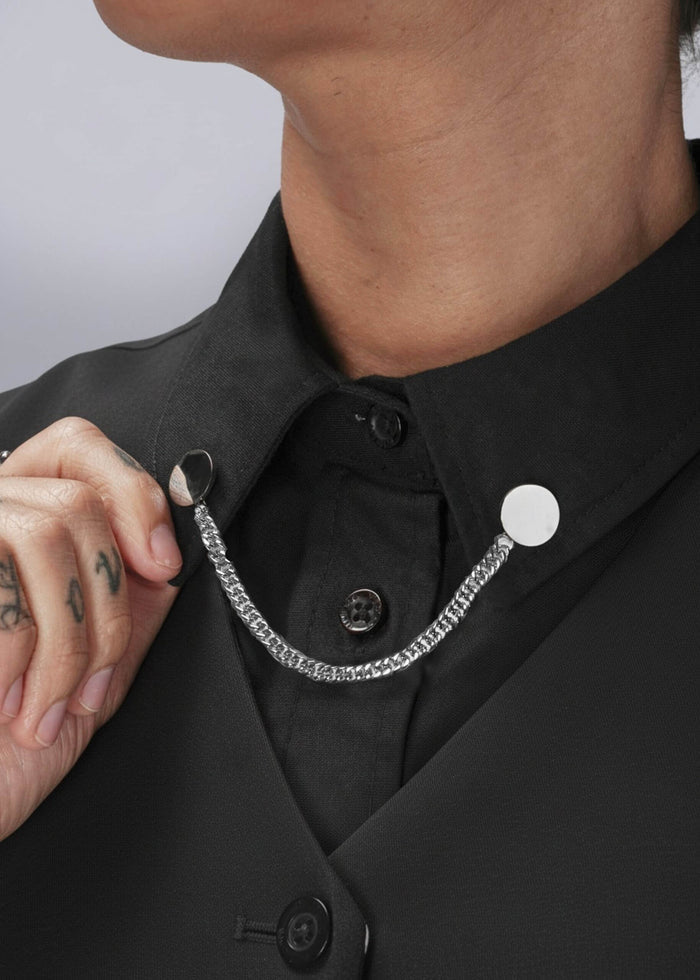 Person wearing a black shirt with silver chain collar clips on a plain background