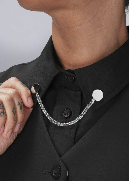 Person wearing a black shirt with silver chain collar clips on a plain background