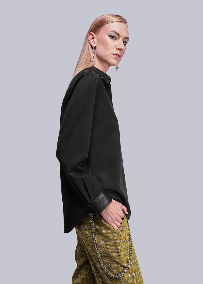 S=Person wearing a black button up shirt and plaid pants against a gray background