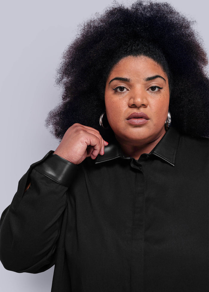 1x=Person wearing a black shirt with vegan leather collar and cuffs on a plain background