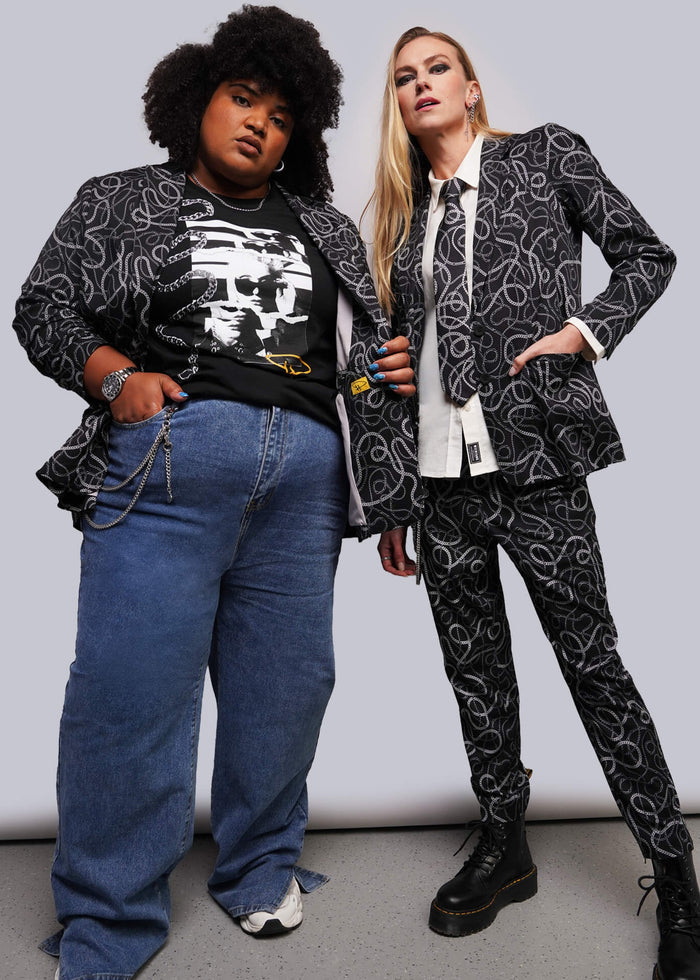Two models posing in matching black and white abstract patterned suits, with one model wearing a black graphic t-shirt and blue jeans, and the other wearing a white collared shirt and tie.