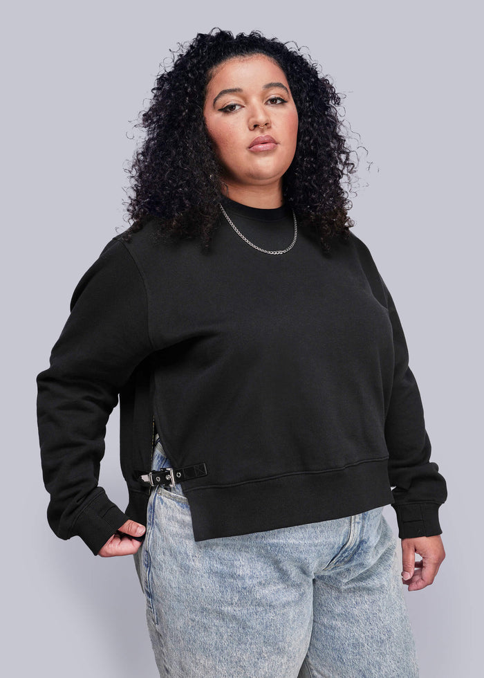 1X=Person wearing a black sweatshirt and light blue jeans against a gray background