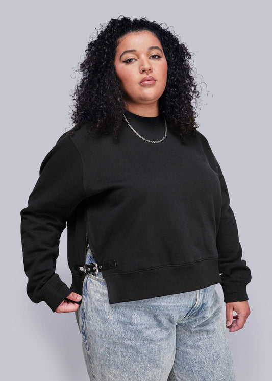 1X=Person wearing a black sweatshirt and light blue jeans against a gray background