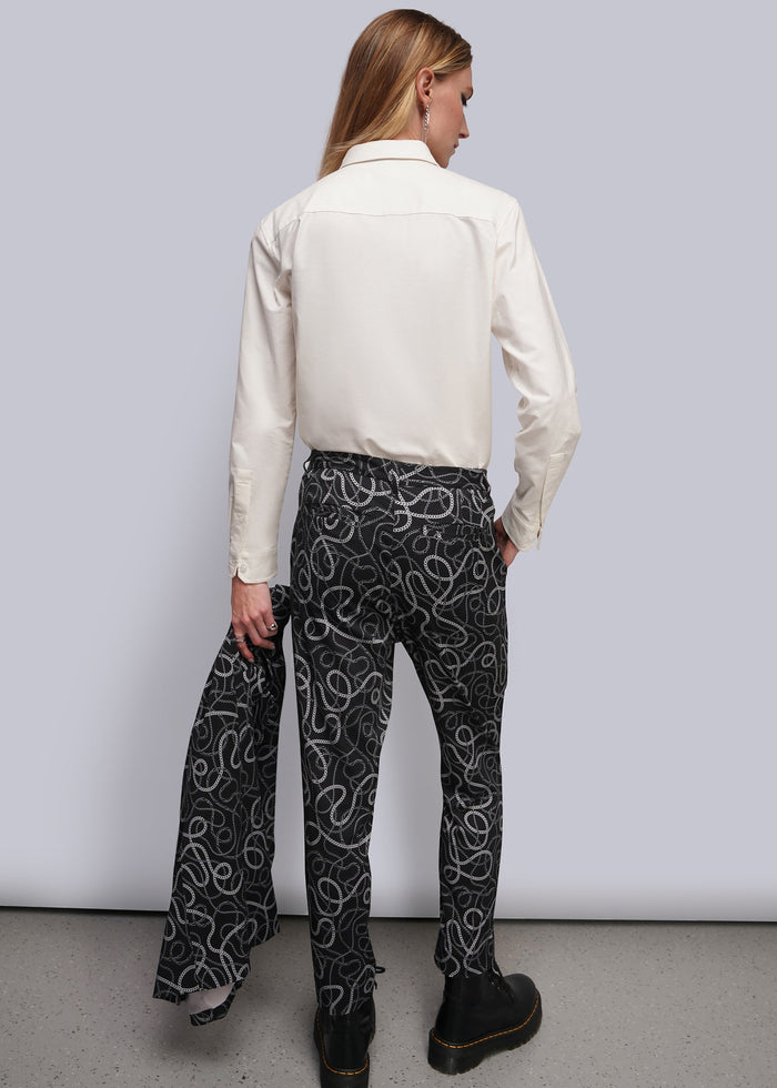 S=A model shown from the back wearing a cream long-sleeve shirt and black trousers with a white chain-link pattern, standing against a light gray studio background.