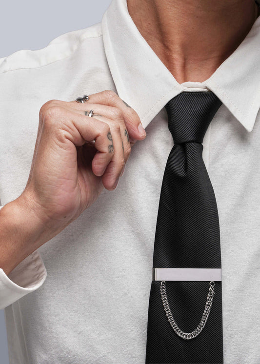 Person adjusting a black tie with a silver tie clip on a white shirt.