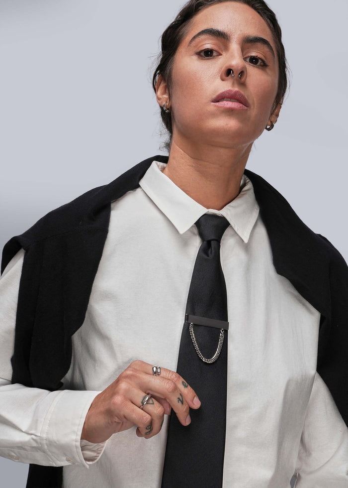 Person wearing a white shirt, black tie with tie clip, and black jacket against a light gray background