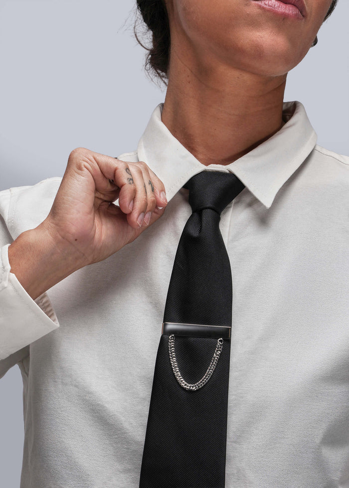 Person adjusting a black tie with a silver tie clip on a white shirt against a light gray background