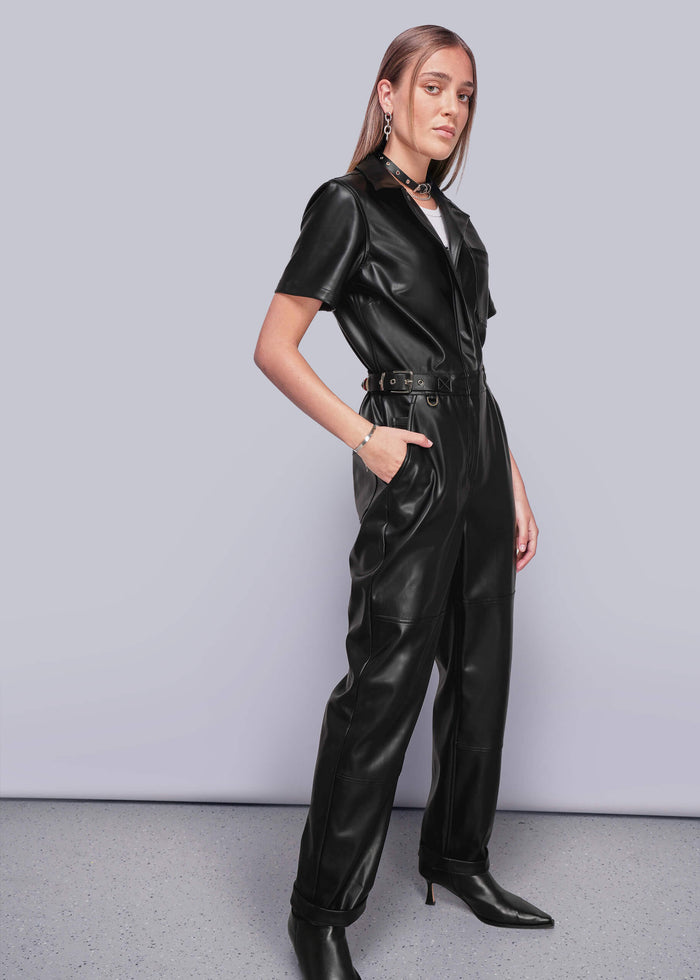 S=Person wearing a black vegan leather jumpsuit against a plain background