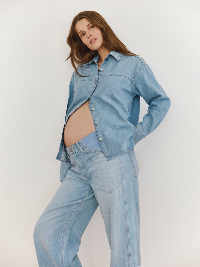 Pregnant woman wearing a light blue denim jacket and jeans on a plain background