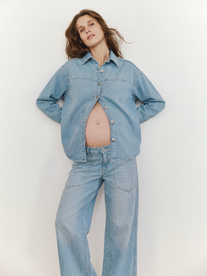 Pregnant woman wearing a denim outfit against a plain background