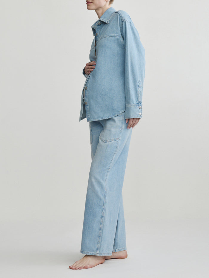 Pregnant woman wearing a light blue denim outfit on a plain background