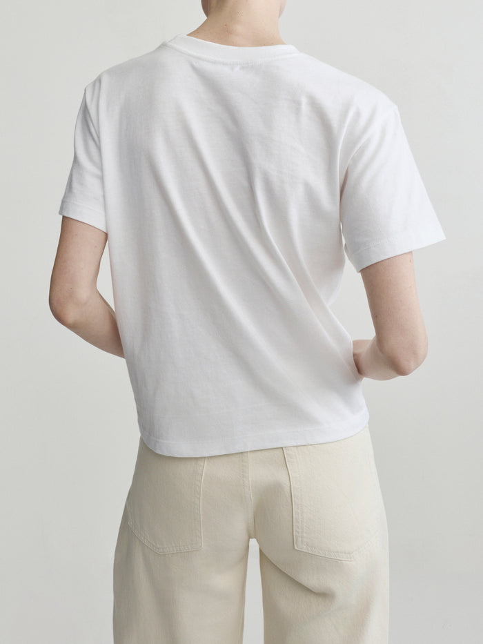Person wearing a plain white t-shirt and beige pants on a light gray background