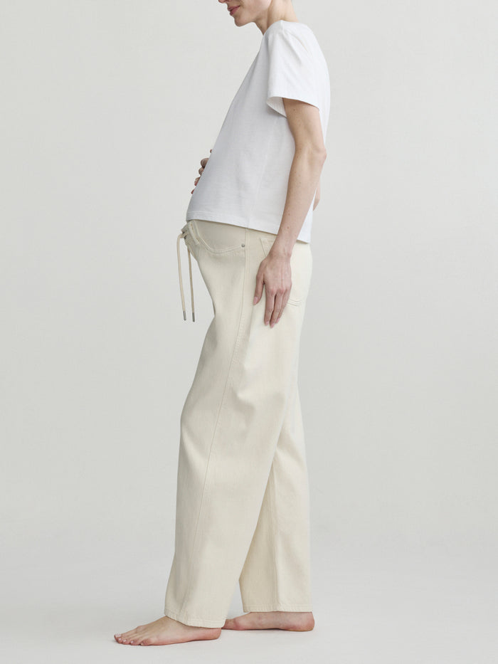 Pregnant person wearing a white t-shirt and beige pants on a plain background