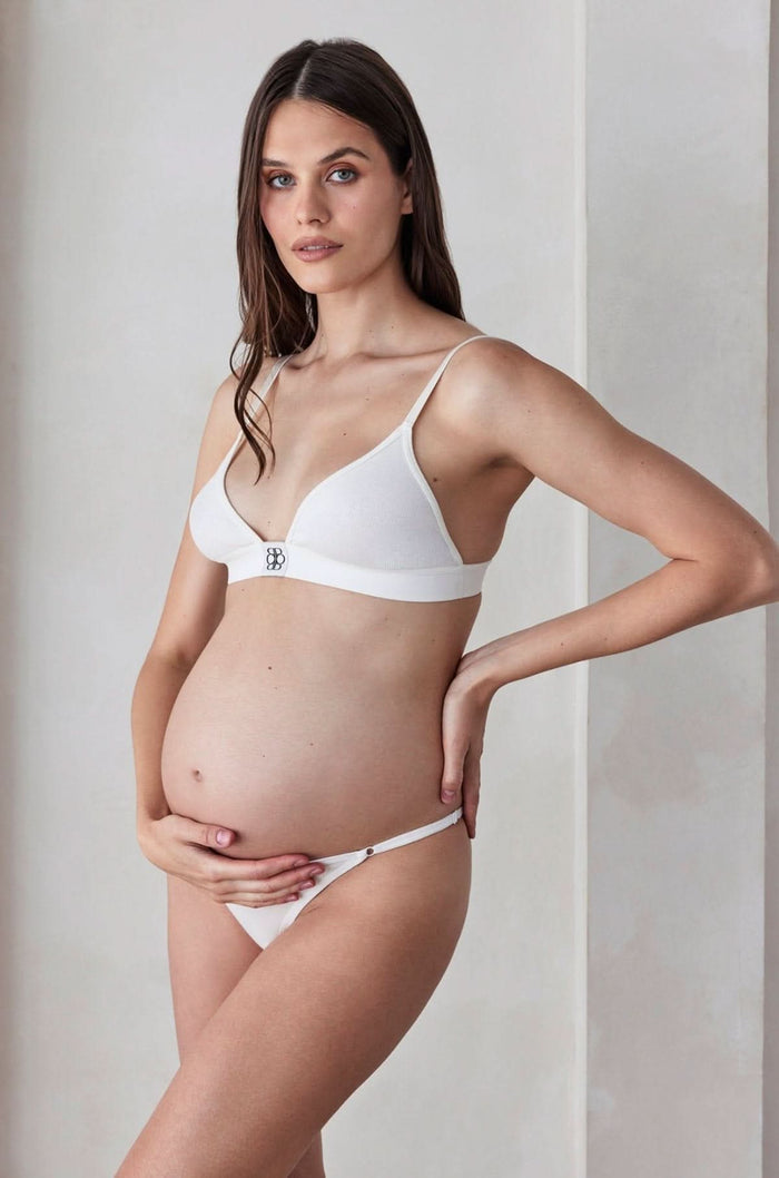 Pregnant woman wearing a white bra and panties set against a plain background