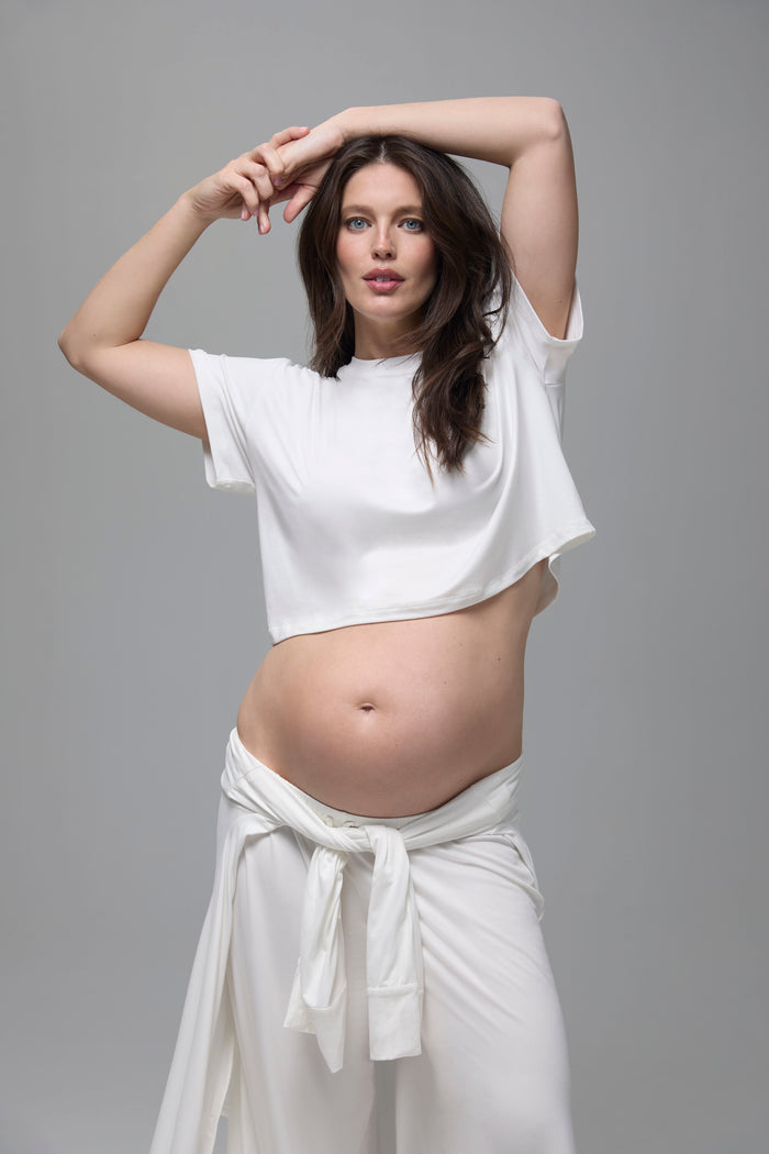 Pregnant woman wearing a white outfit against a gray background