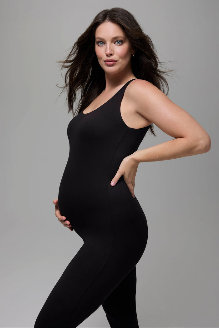 Pregnant woman wearing a black jumpsuit against a grey background