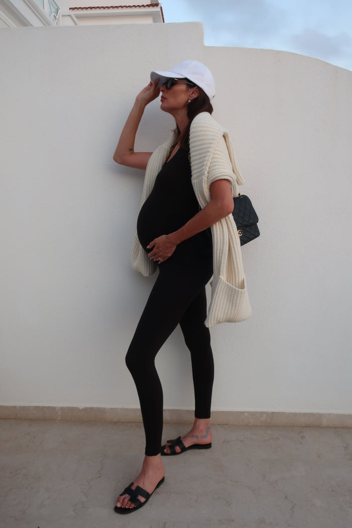 Pregnant person leaning against a white wall with a neutral expression