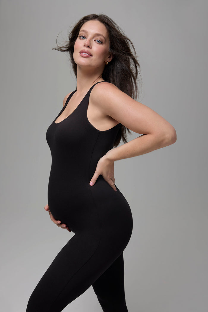 Woman wearing a Bumpsuit black bodysuit against a gray background