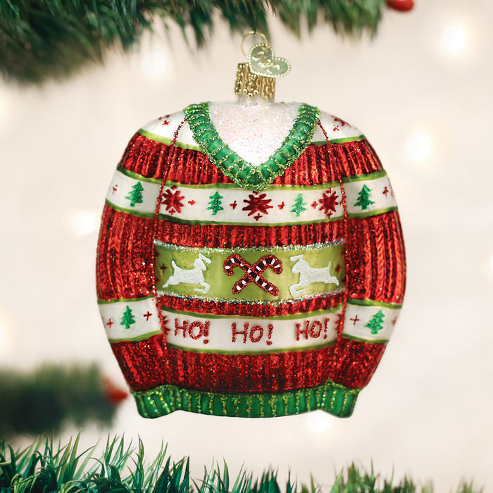 A Christmas tree ornament shaped like a red and green sweater with glitter, featuring reindeer, Christmas trees, candy canes, and the words HO! HO! HO! hanging from a branch.
