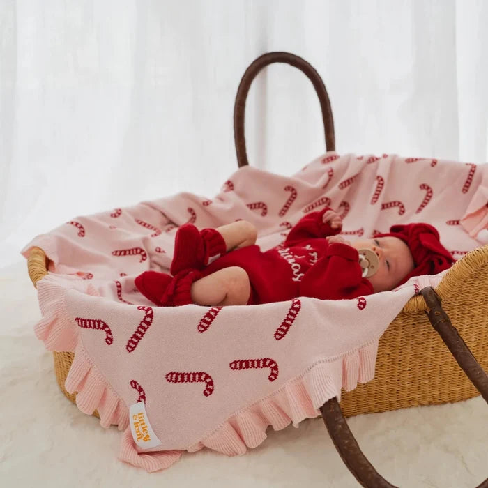 Baby in a woven basket with a pink knit blanket featuring candy cane pattern