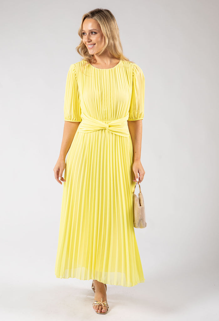 Woman wearing a yellow pleated dress holding a beige handbag on a white background