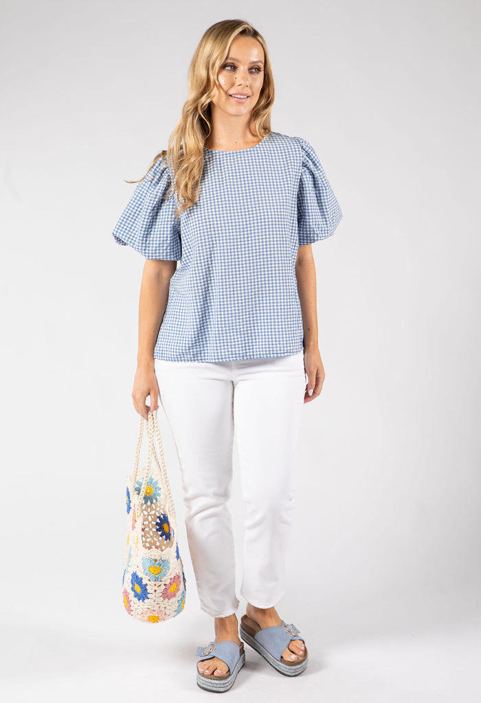 Woman wearing a blue checkered top and white pants, holding a floral bag on a white background