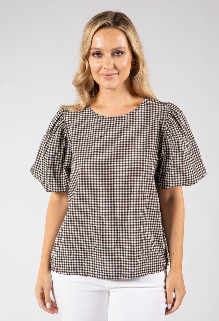 Woman wearing a brown and white checkered blouse against a plain background