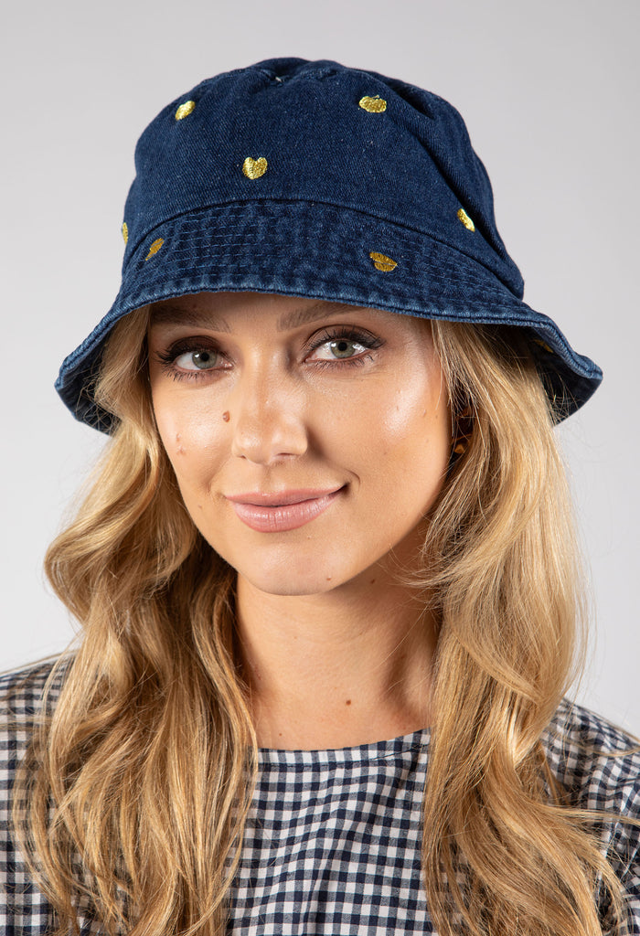 Woman wearing a blue denim bucket hat with gold buttons on a gray background