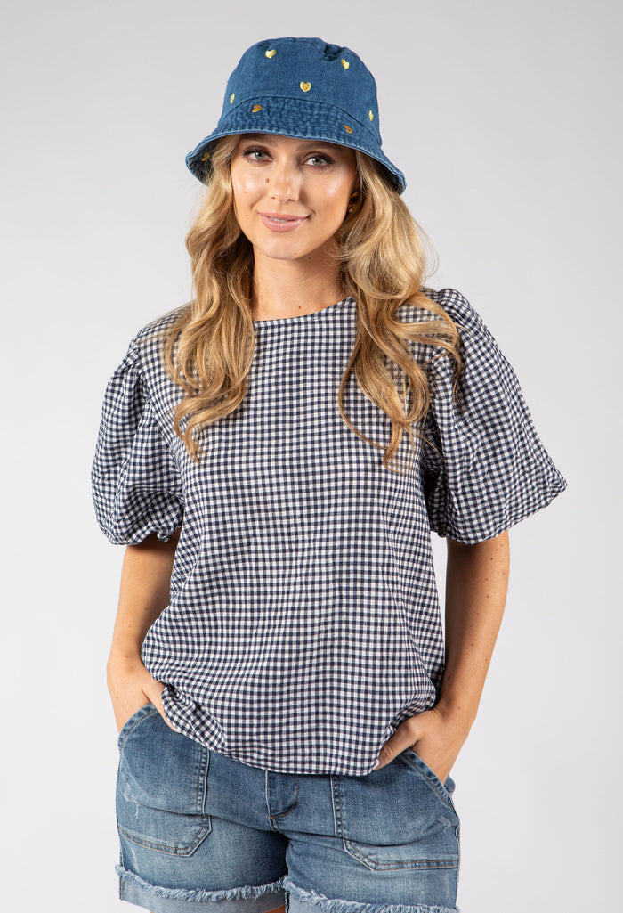 Woman wearing a checkered top, denim shorts, and a denim bucket hat on a white background