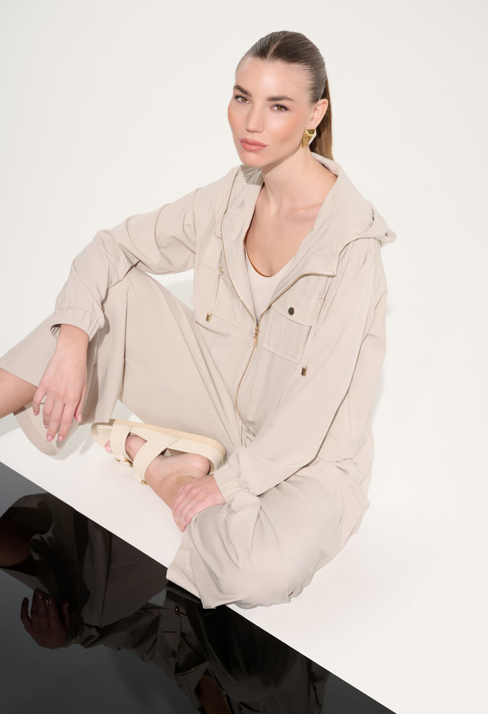 Woman wearing a beige outfit sitting on a white surface with a plain background