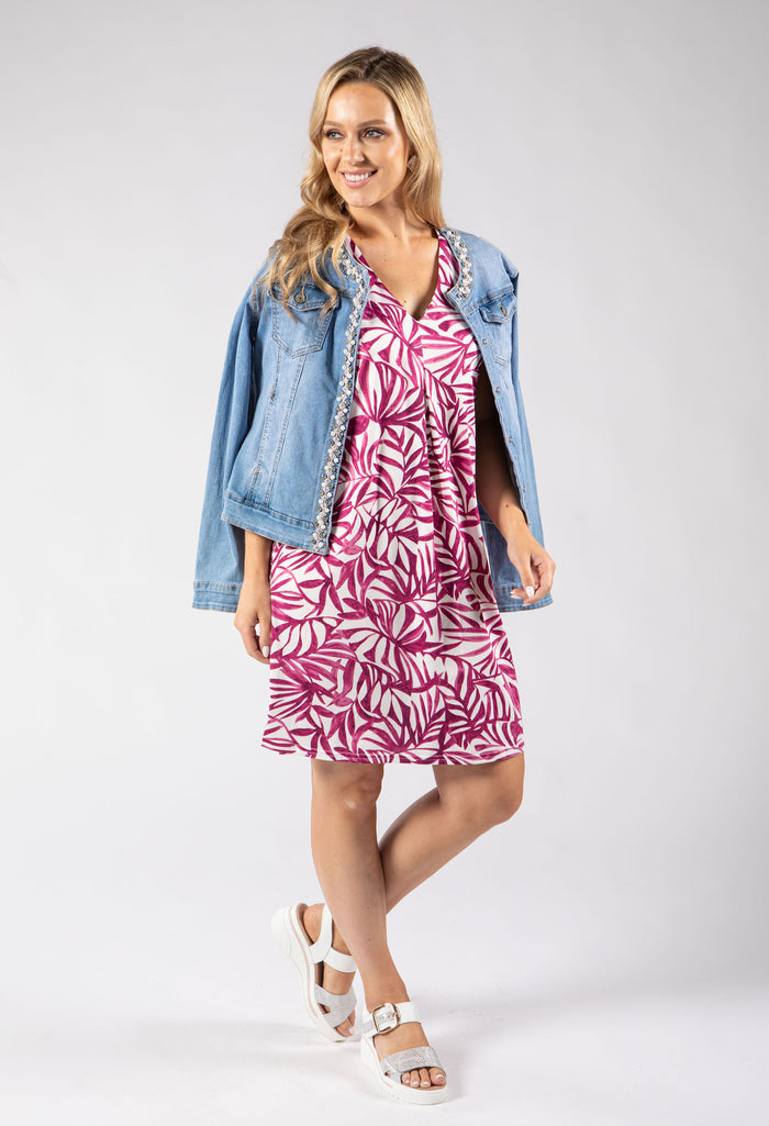 Woman wearing a pink leaf-patterned dress with a denim jacket on a white background